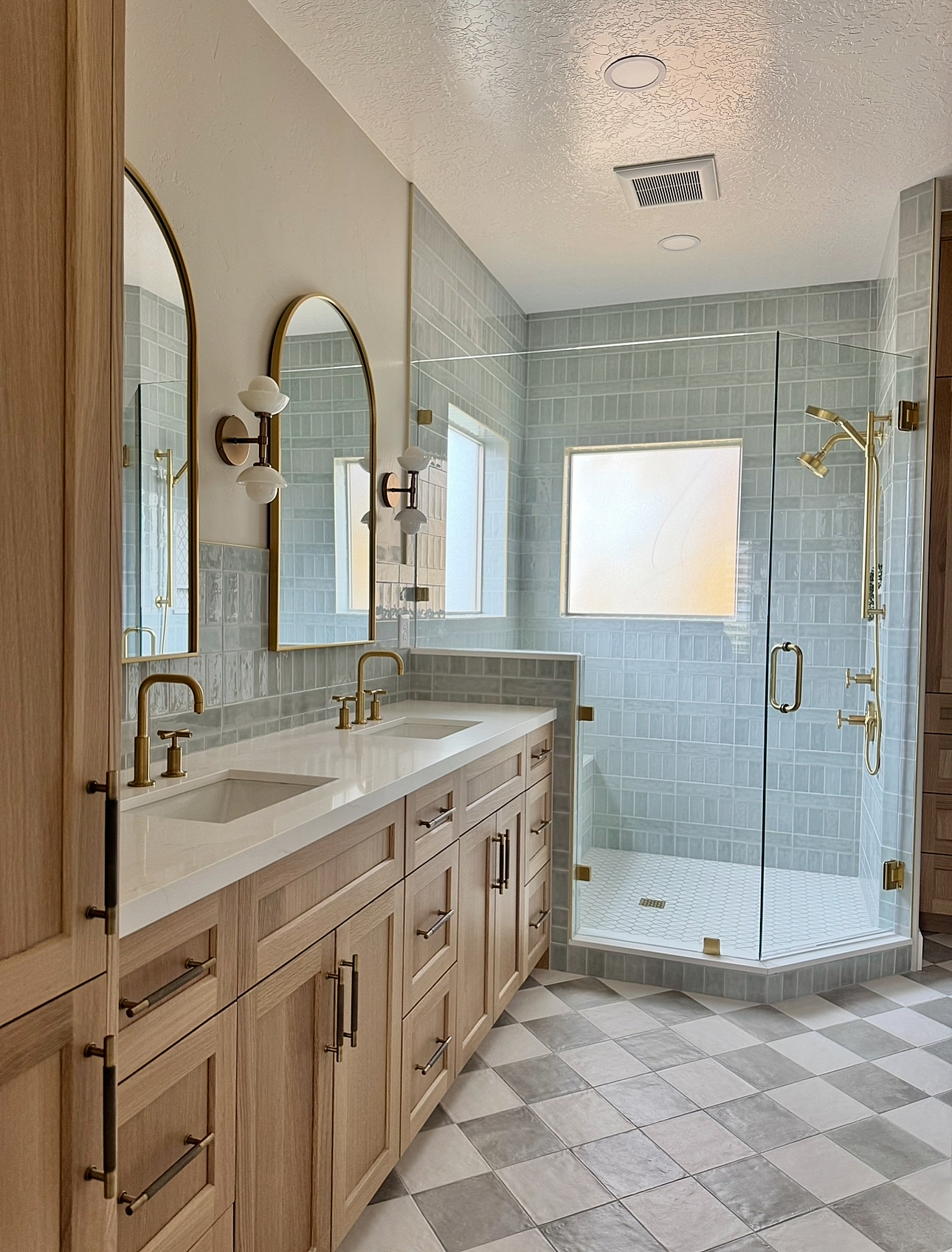 Primary bathroom remodel with blue tile shower, double vanity and brass fixtures