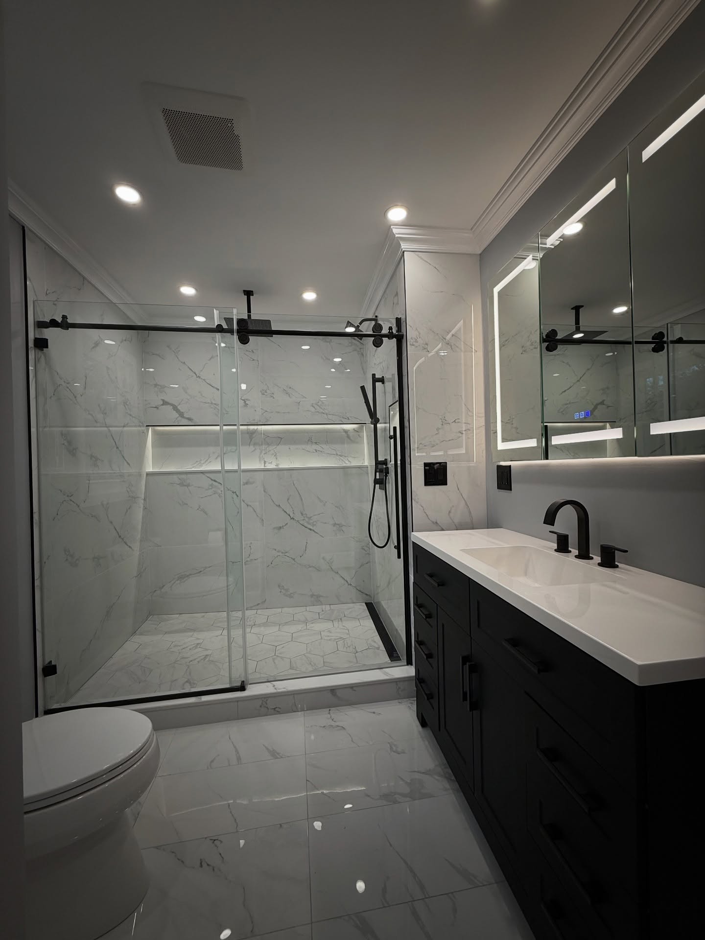 Bathroom remodel with marble-look tile, black fixtures and a lighted mirror