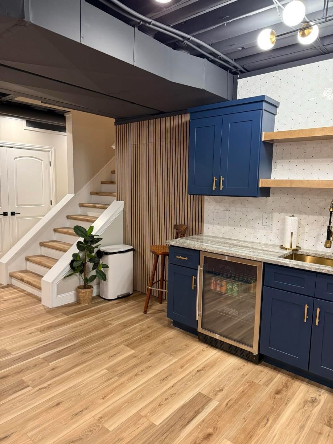 Finished basement with navy wet bar, slat wall and beverage cooler