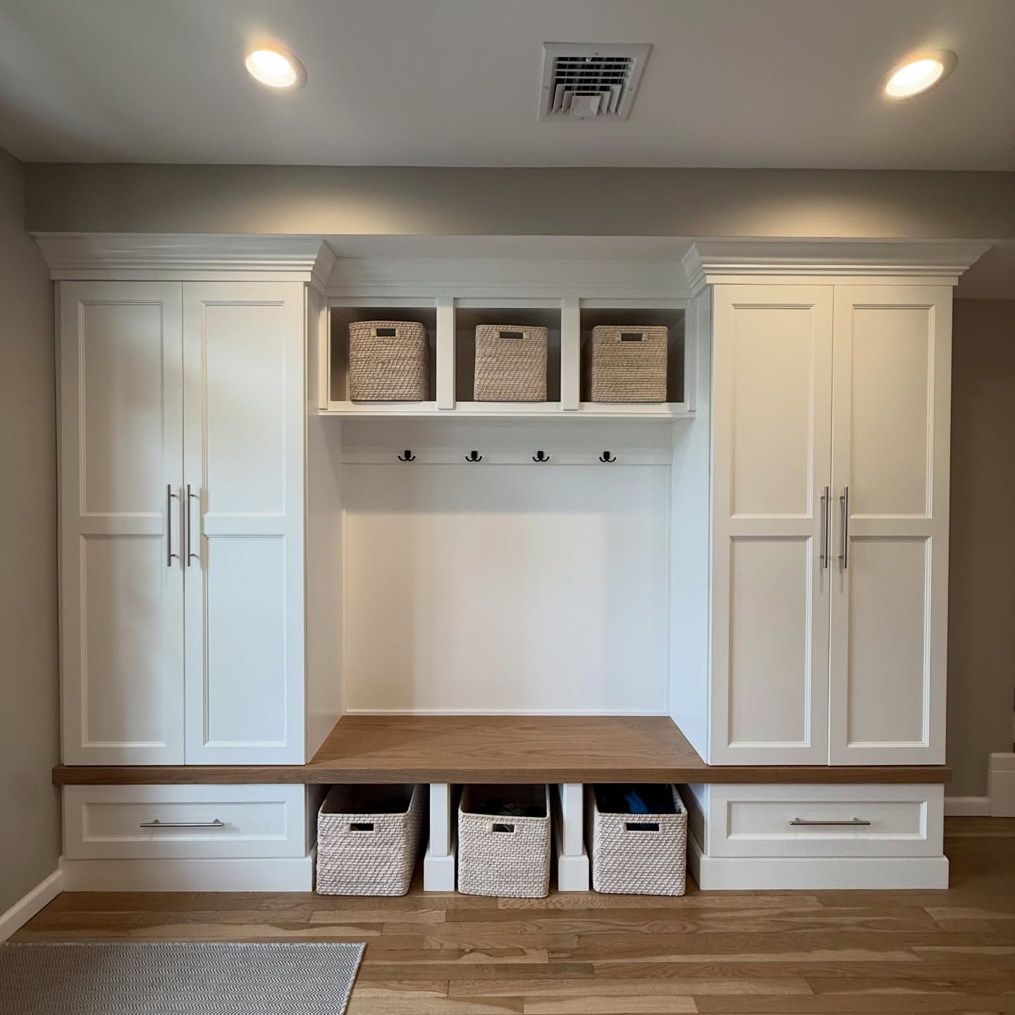 White mudroom built-in with cubby baskets, hooks and a wood bench